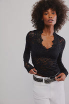 Woman wearing a black lace top and white pants against a plain background