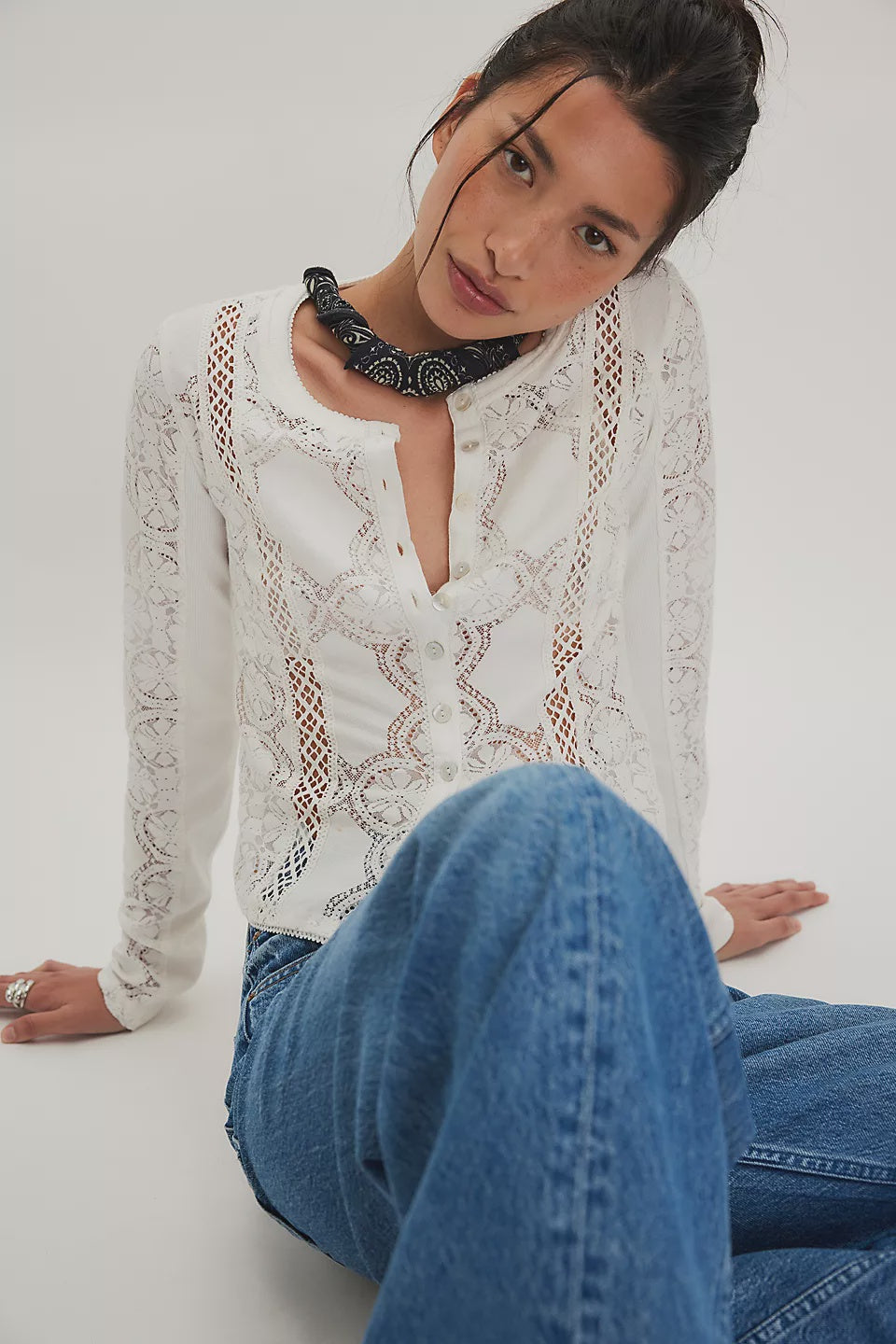 Woman wearing a white lace top and blue jeans sitting on a white background