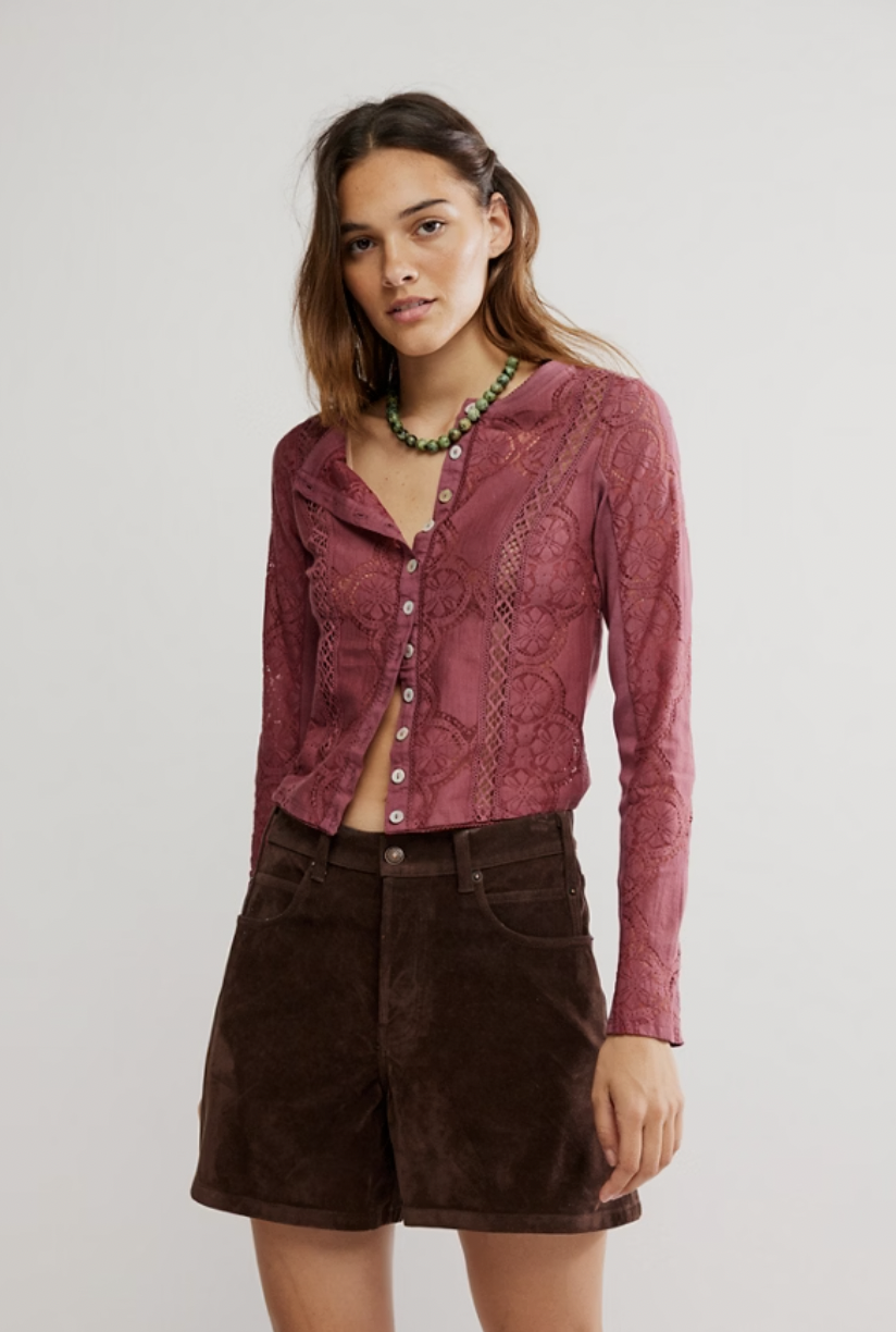Woman wearing a burgundy lace shirt and brown shorts on a plain background
