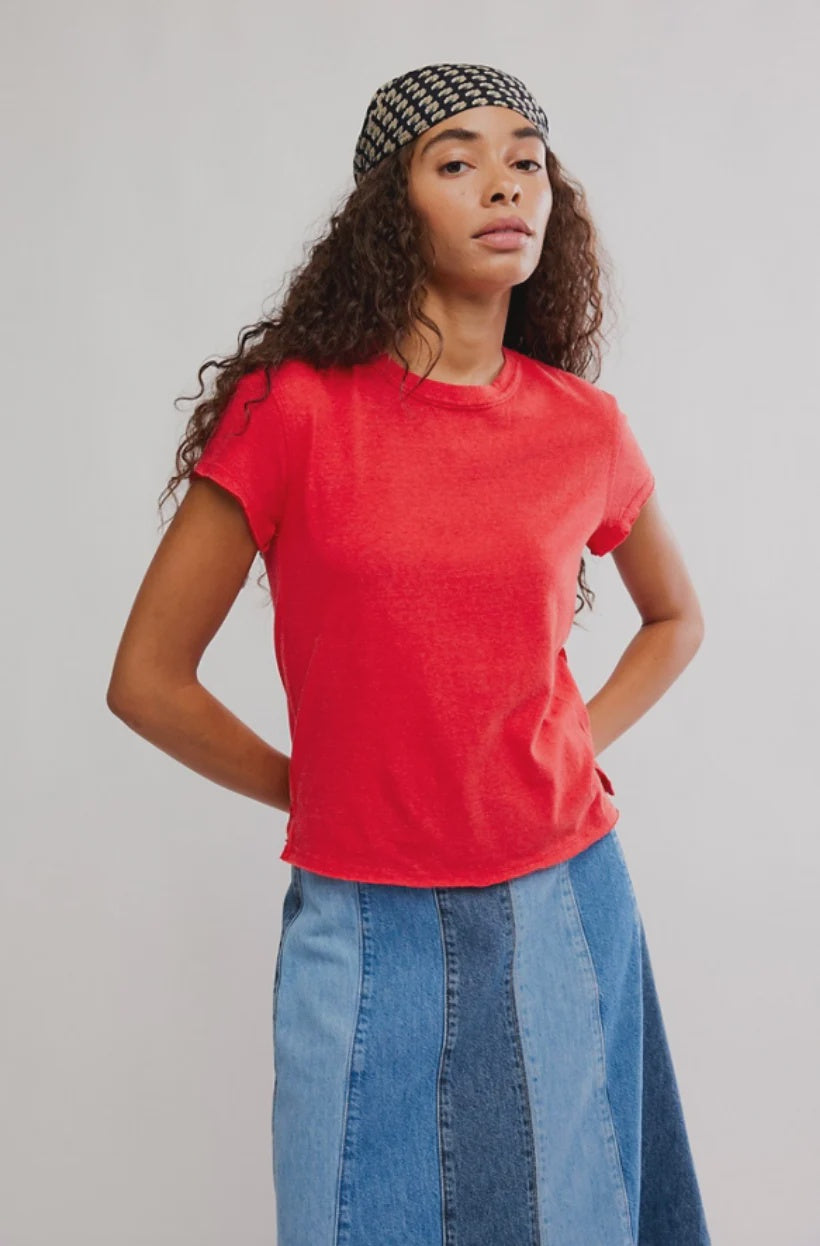 Woman wearing a red shirt and blue denim skirt against a plain background