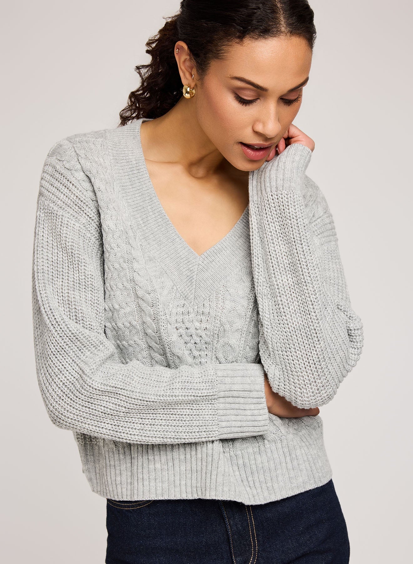 Woman wearing a light gray cable knit sweater against a plain background