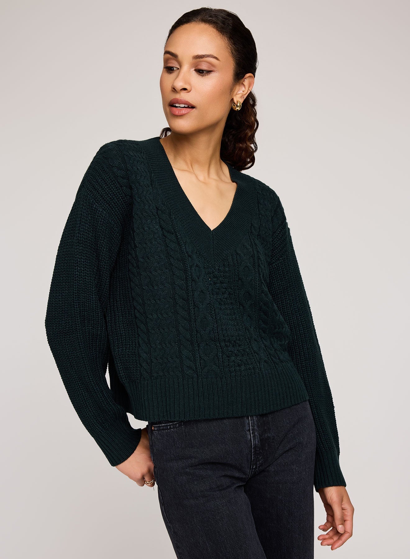 Woman wearing a dark green cable knit sweater against a plain background