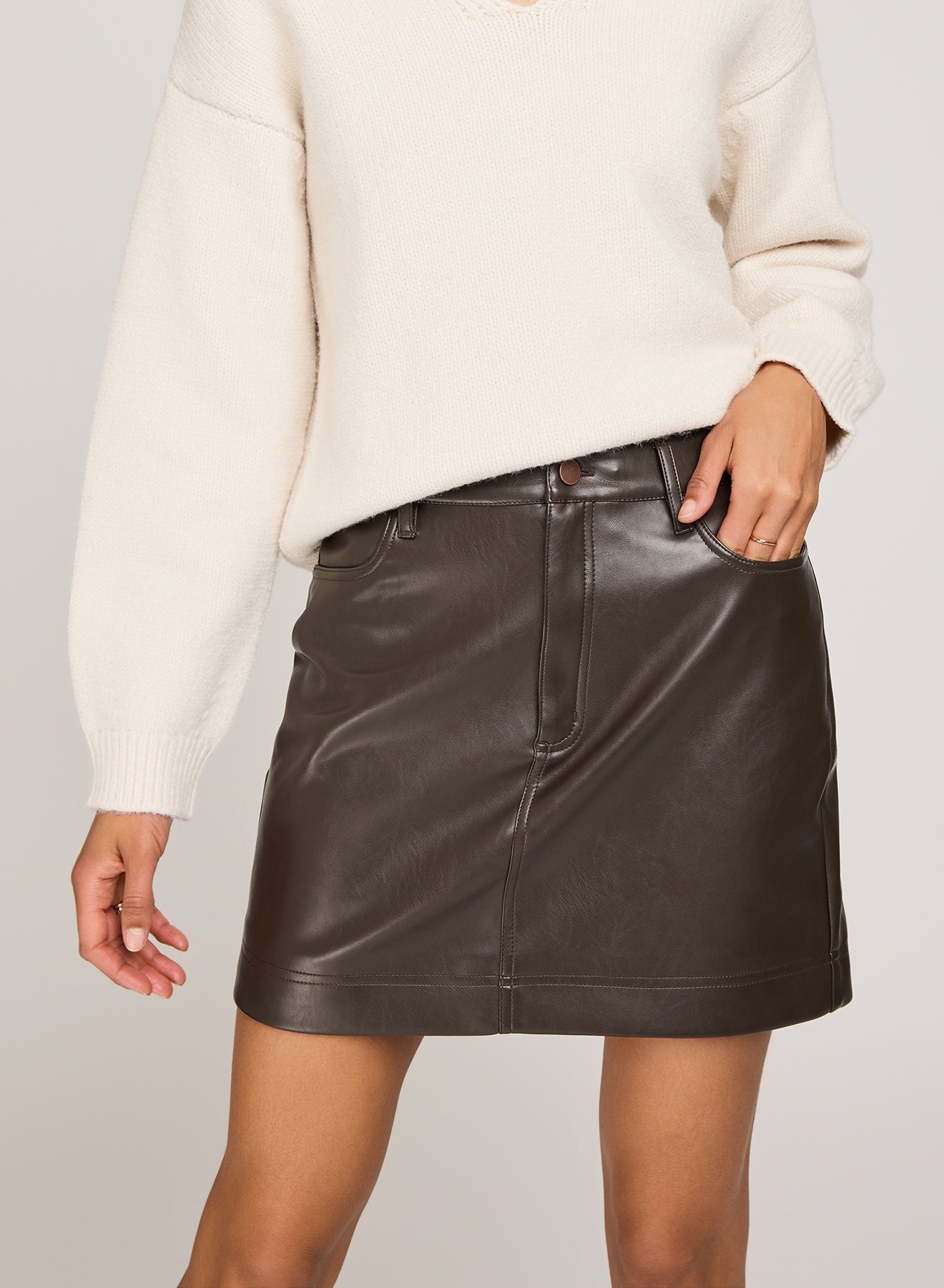 Person wearing a black leather skirt with a white sweater on a plain background