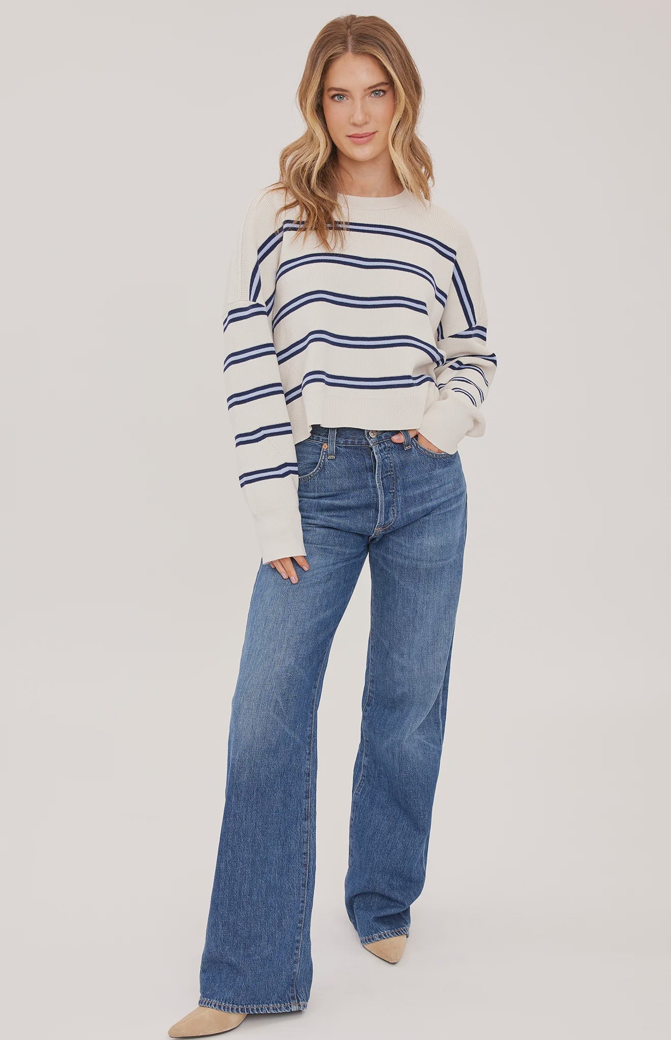 Woman wearing the Gentle Fawn Echo Sweater in Cream Stripe, featuring a super soft knit, oversized fit, half-cardigan stitch, exposed seam detailing, side slits, and classic cream striped pattern.