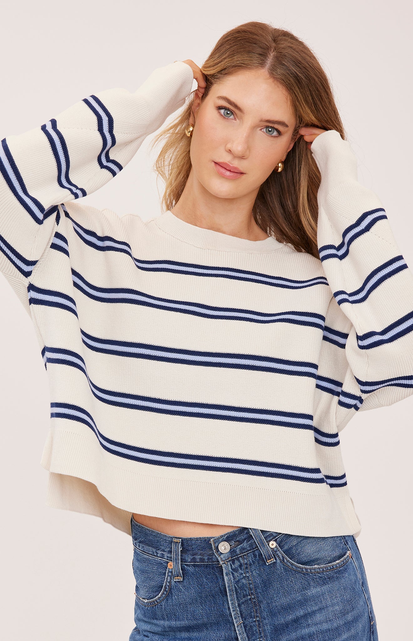 Woman wearing the Gentle Fawn Echo Sweater in Cream Stripe, featuring a super soft knit, oversized fit, half-cardigan stitch, exposed seam detailing, side slits, and classic cream striped pattern.