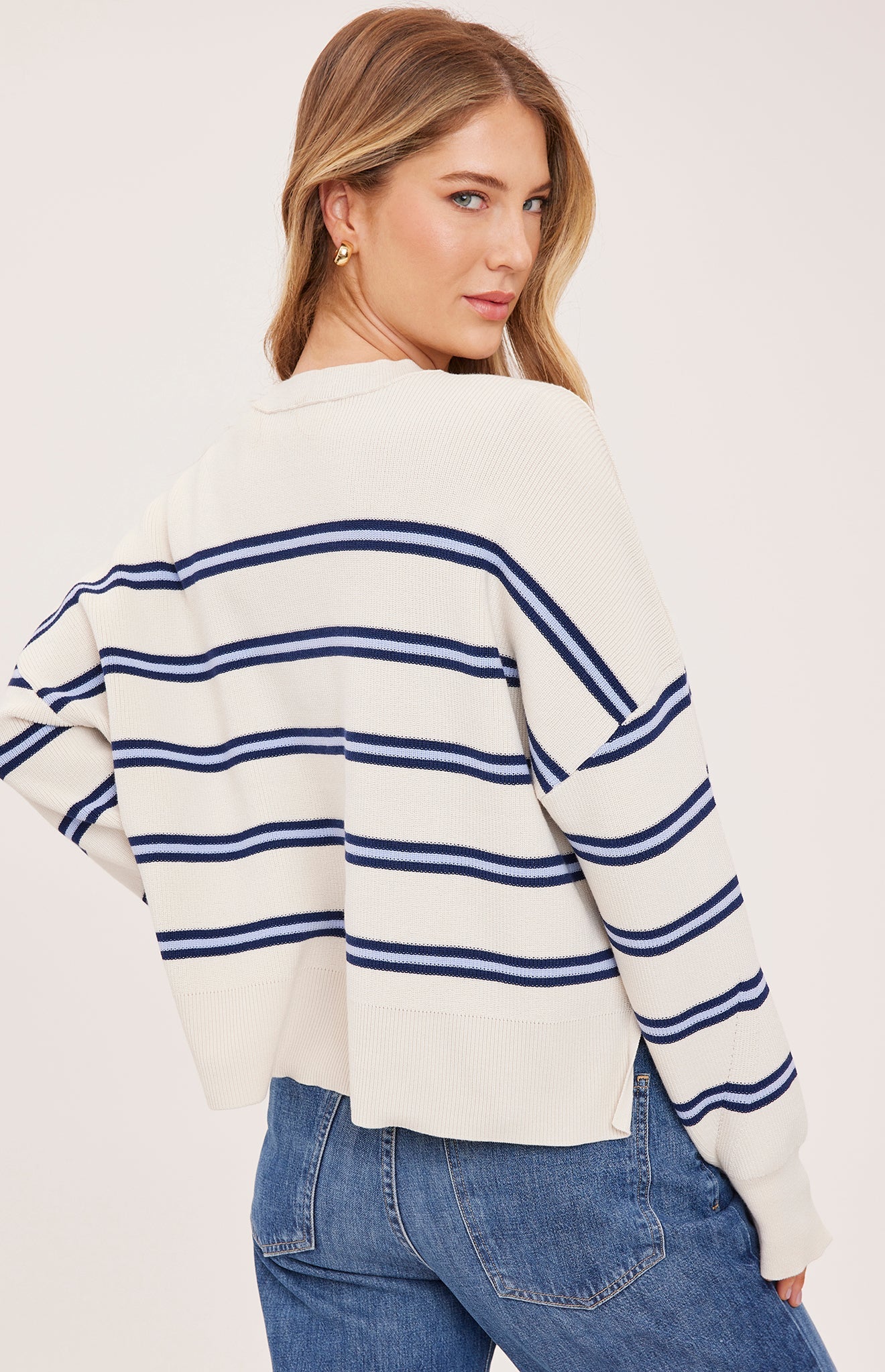Woman wearing the Gentle Fawn Echo Sweater in Cream Stripe, featuring a super soft knit, oversized fit, half-cardigan stitch, exposed seam detailing, side slits, and classic cream striped pattern.
