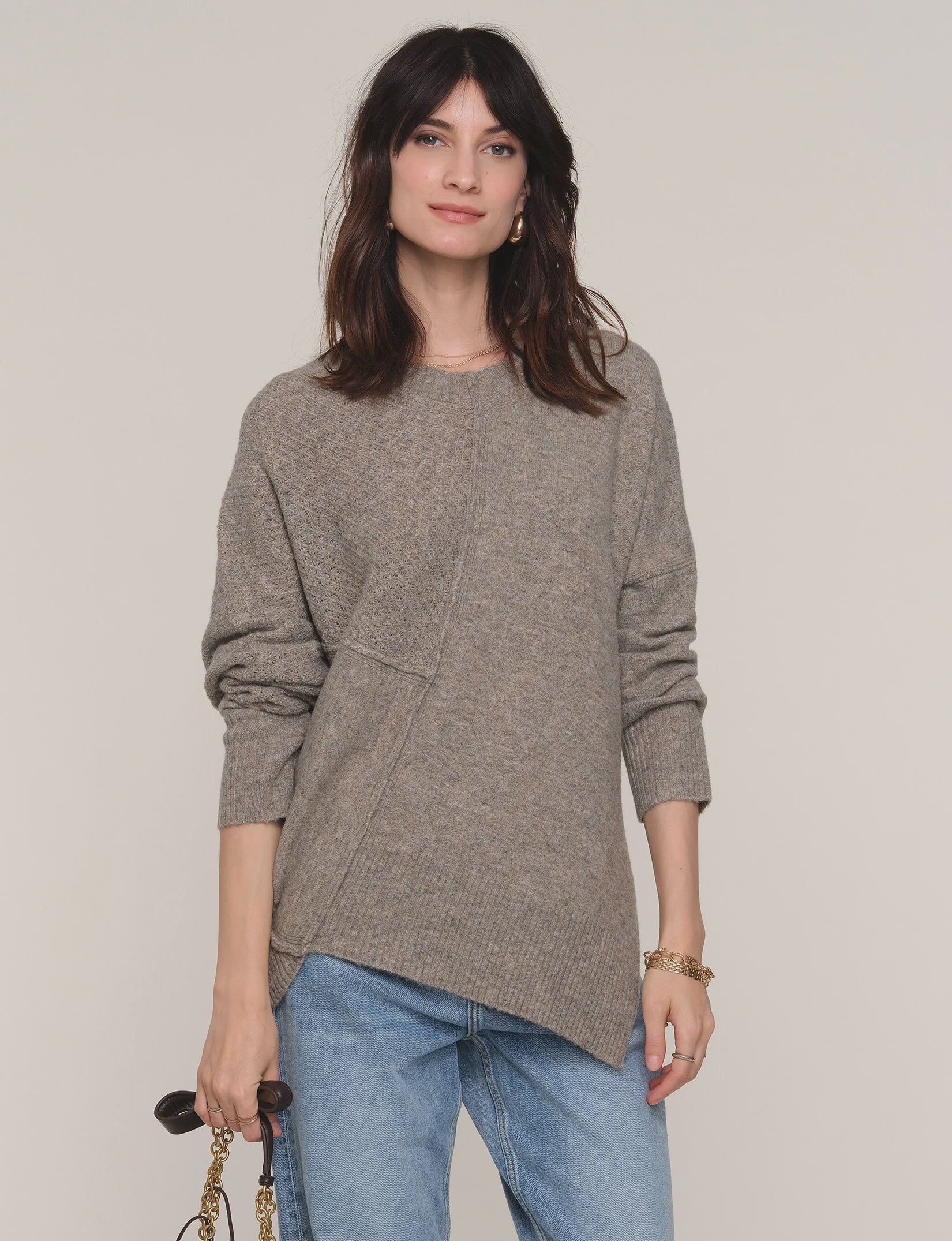 Woman wearing a gray sweater and blue jeans against a plain background