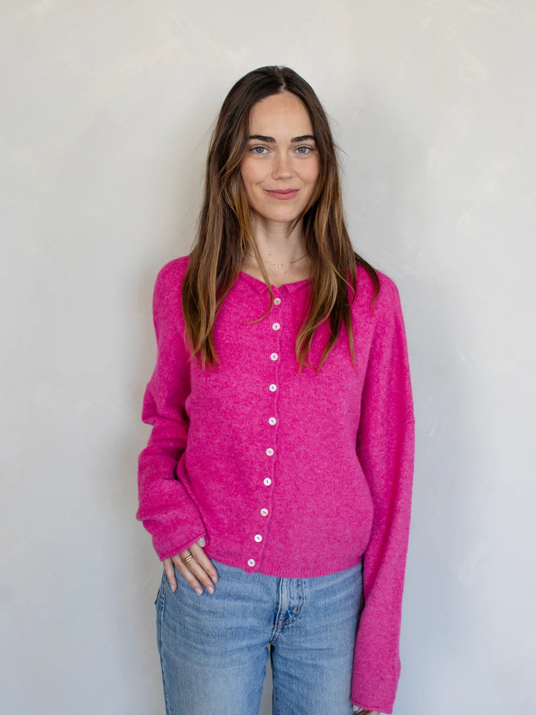 Woman wearing a bright pink cardigan against a plain background