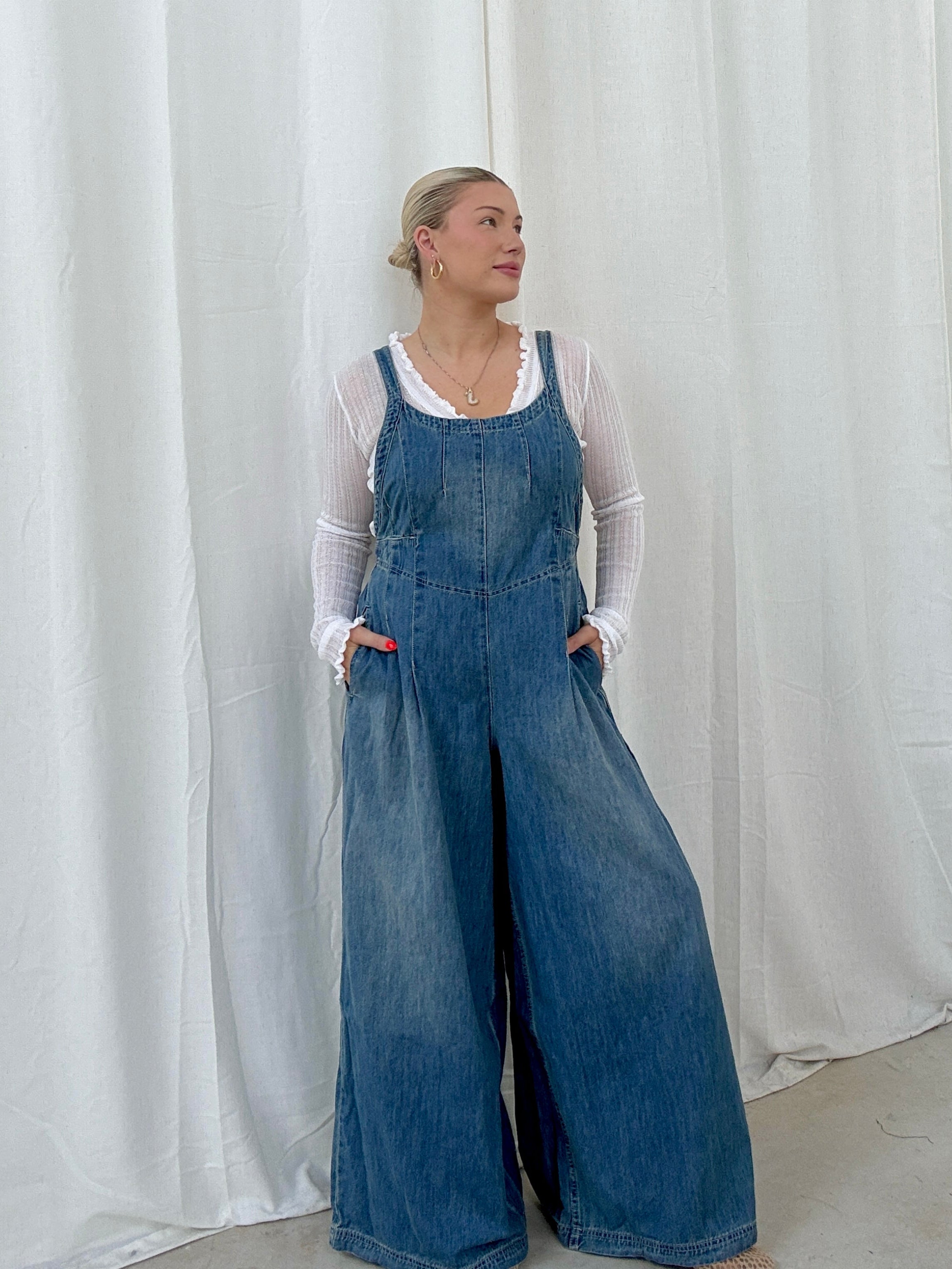Person wearing blue denim overalls against a white curtain background