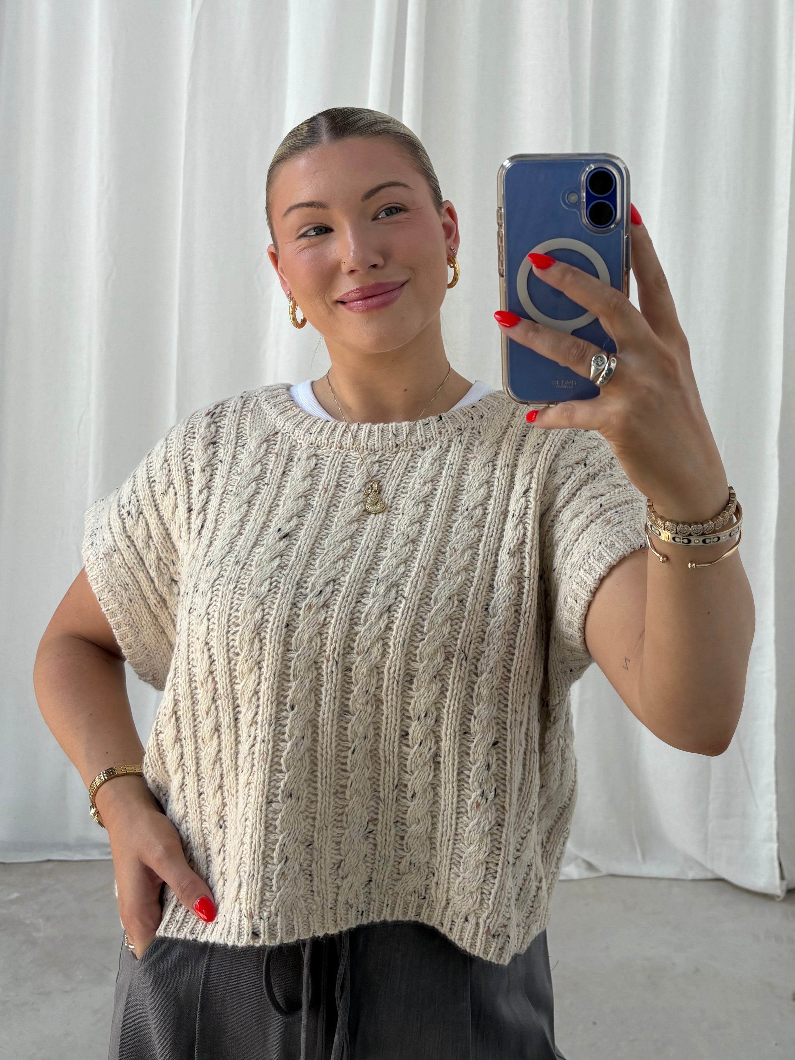Person taking a mirror selfie wearing a textured top and holding a phone.