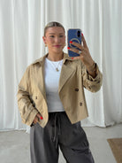 Person wearing a beige trench coat in front of a white curtain