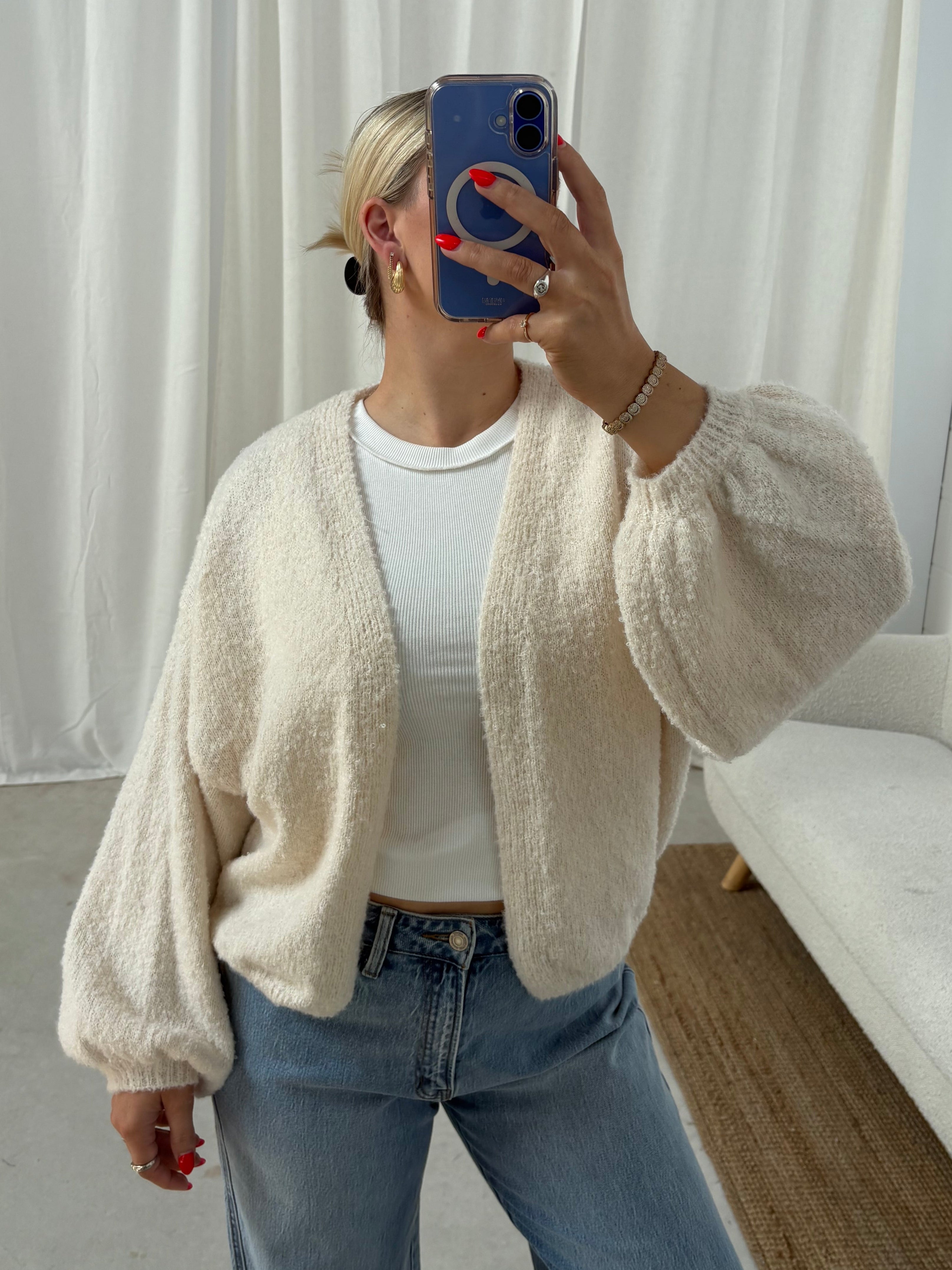 Person taking a mirror selfie wearing a beige cardigan and blue jeans.