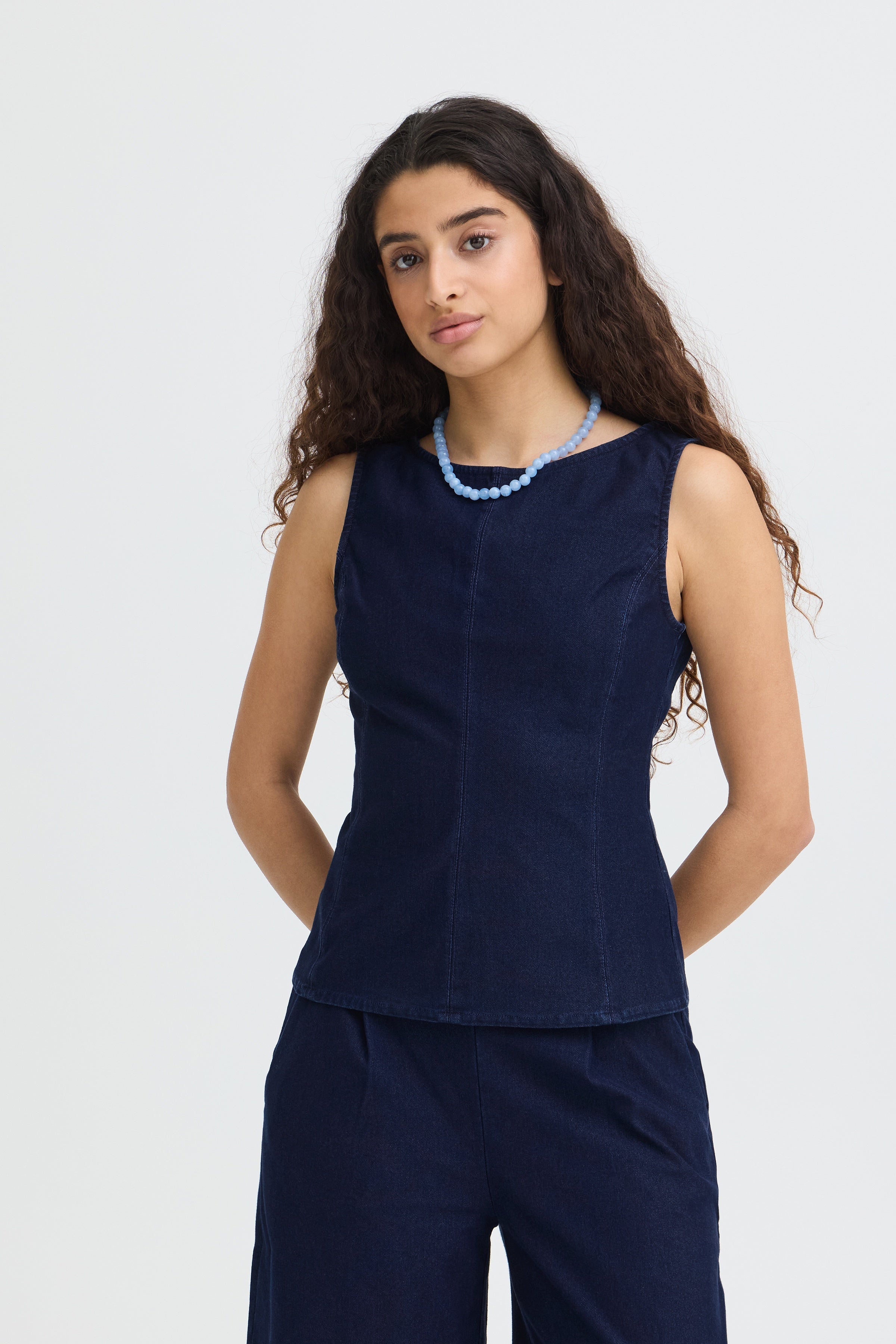 Woman wearing a navy sleeveless top and pants with a white background