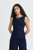 Woman wearing a navy sleeveless top and pants with a white background