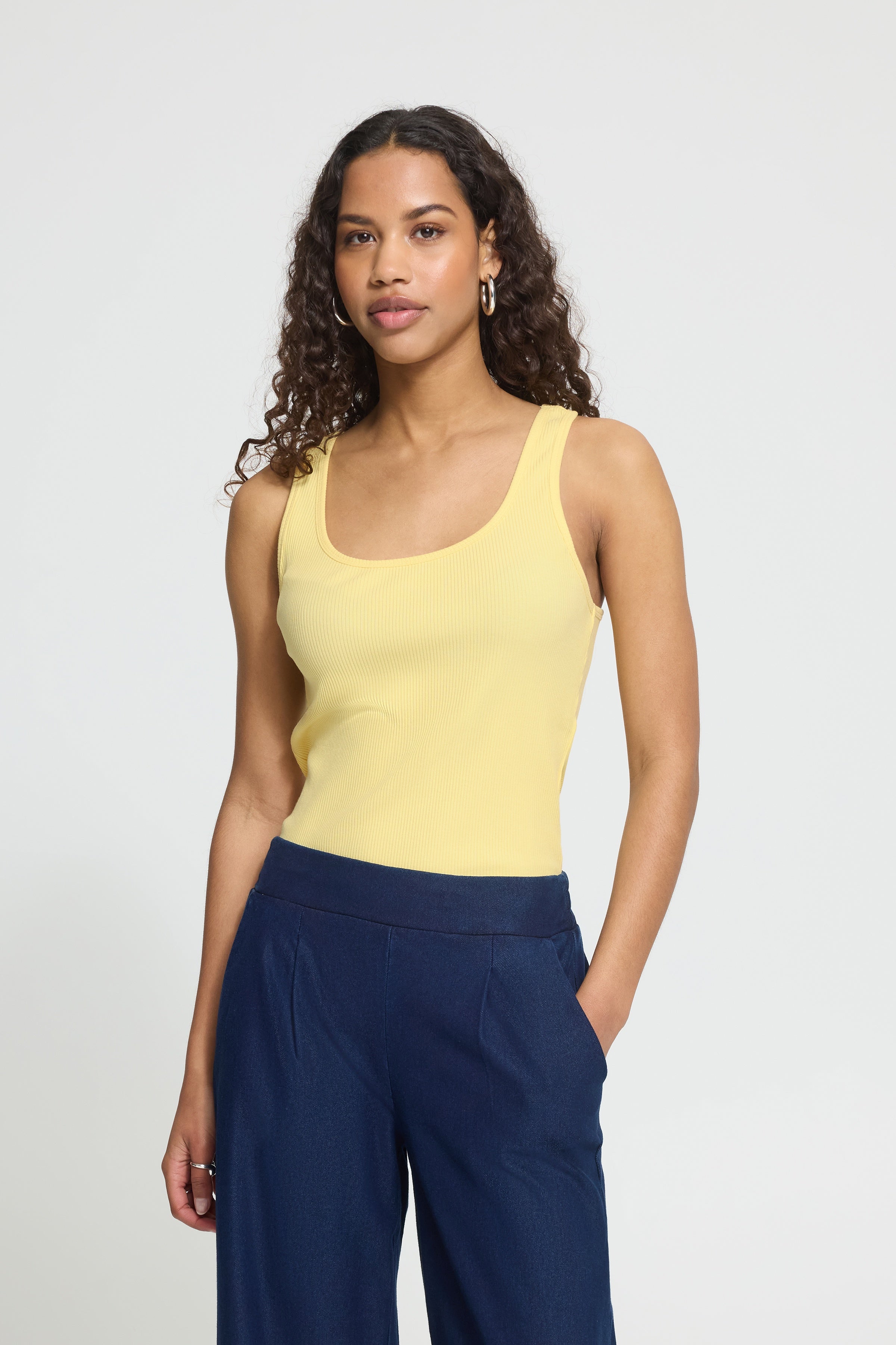 Woman wearing a yellow tank top and navy pants against a plain background