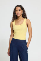 Woman wearing a yellow tank top and navy pants against a plain background