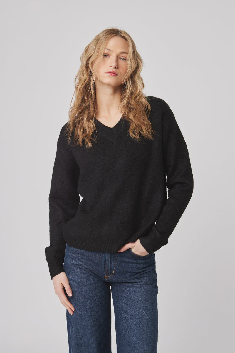 Woman wearing a black sweater and blue jeans against a plain background