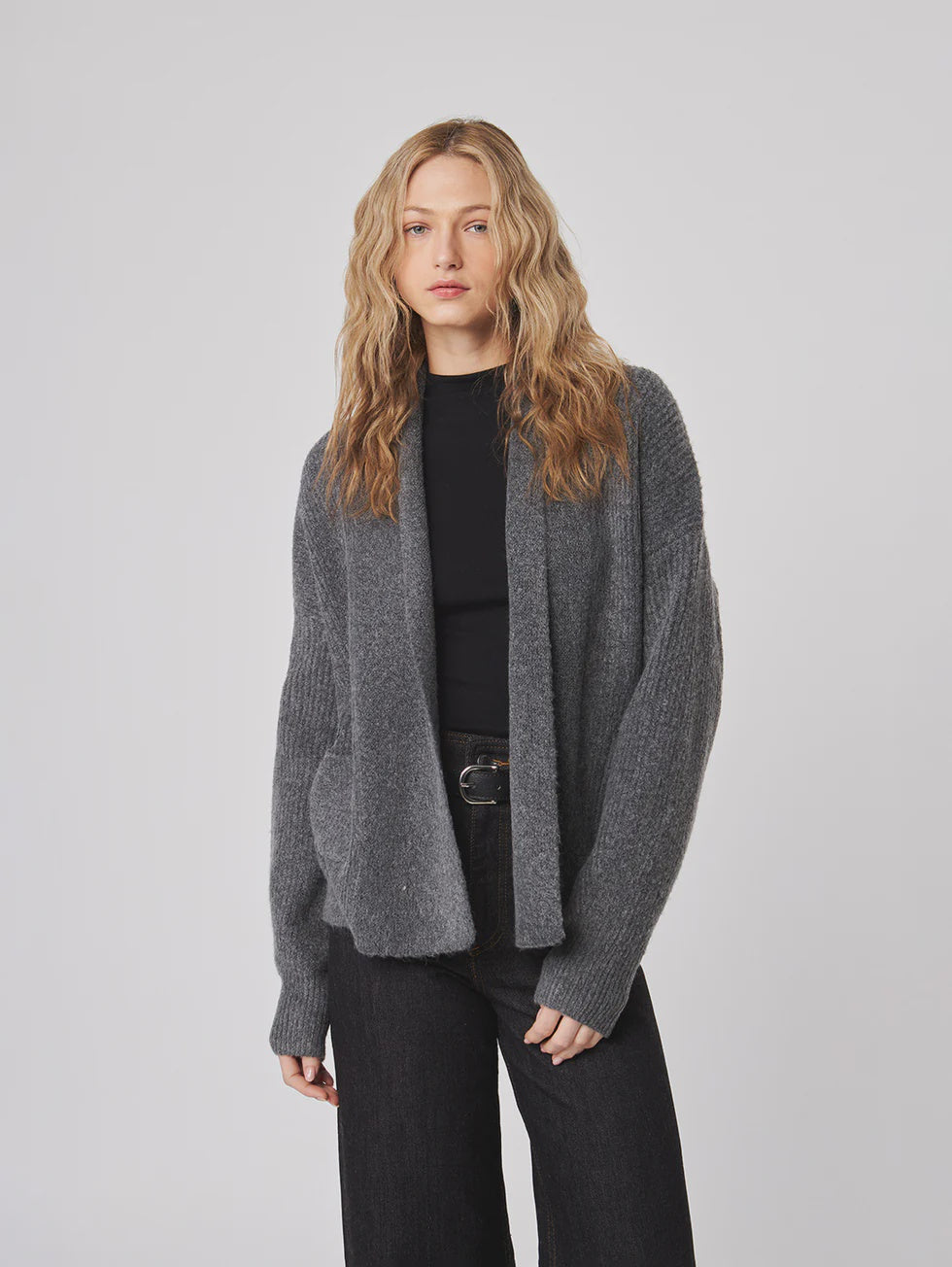 Woman wearing a gray cardigan over a black top and pants on a light gray background