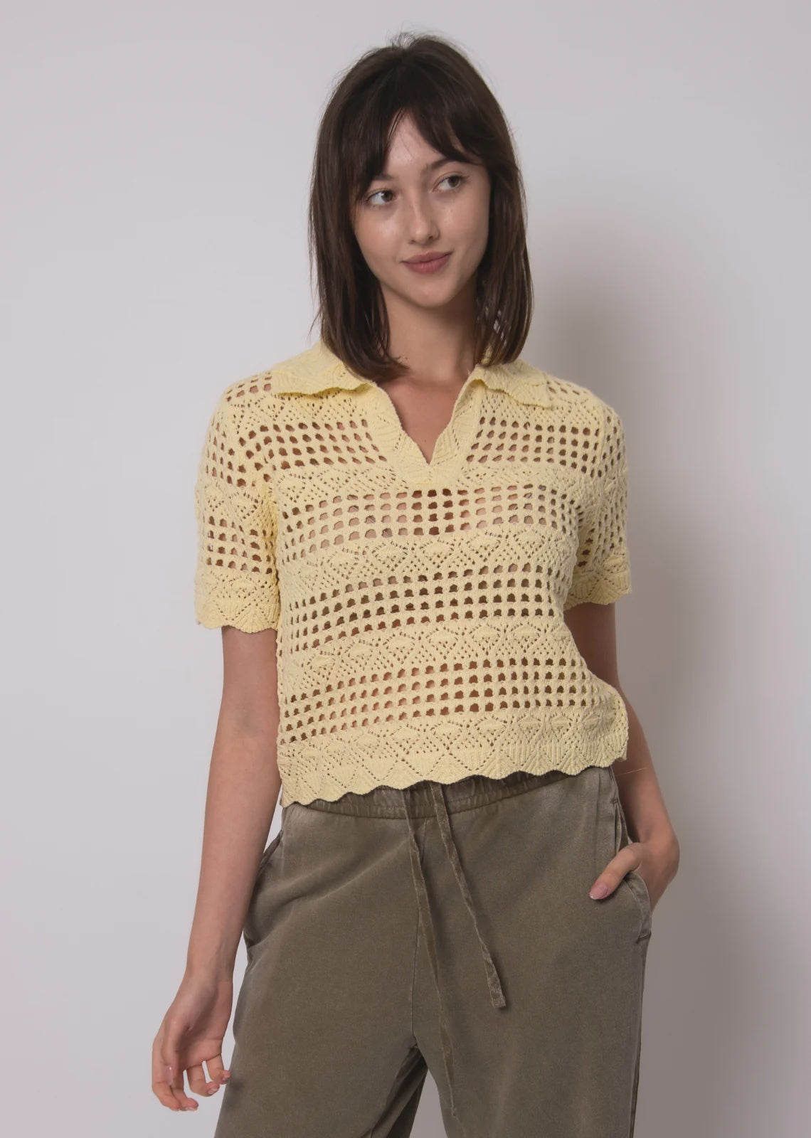 Woman wearing a yellow crochet top against a plain background