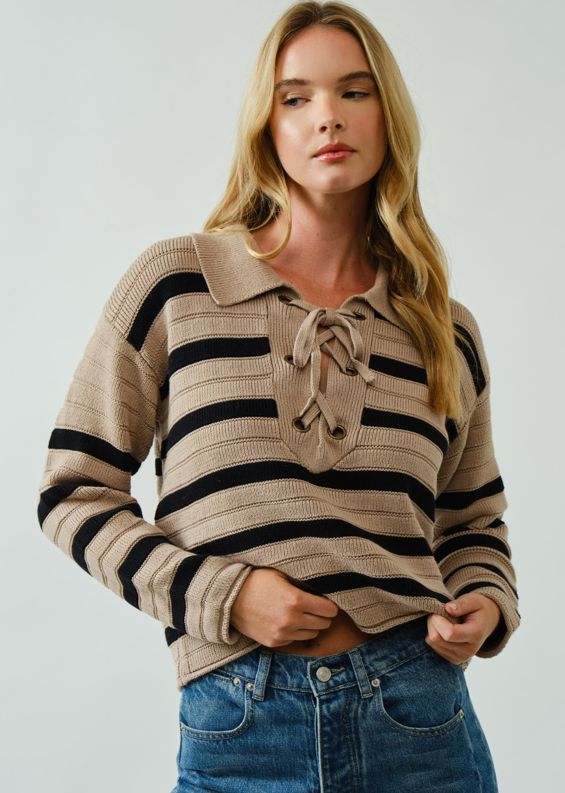 Woman wearing a striped sweater with a collar and tie detail on a plain background