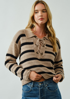 Woman wearing a striped sweater with a collar and tie detail on a plain background