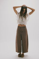 Woman wearing a white lace top and brown wide-leg pants on a white background
