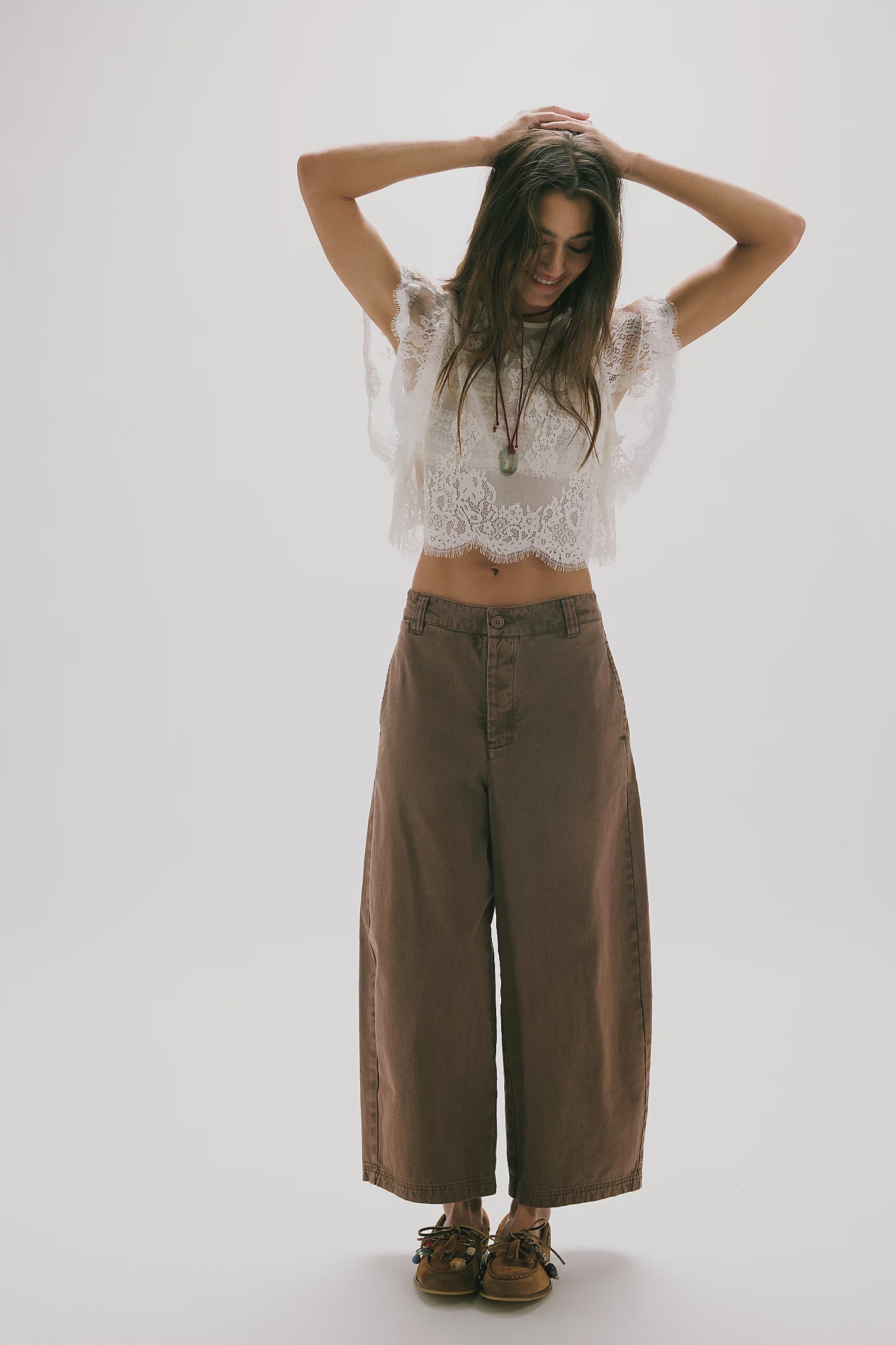 Woman wearing a white lace top and brown wide-leg pants on a white background