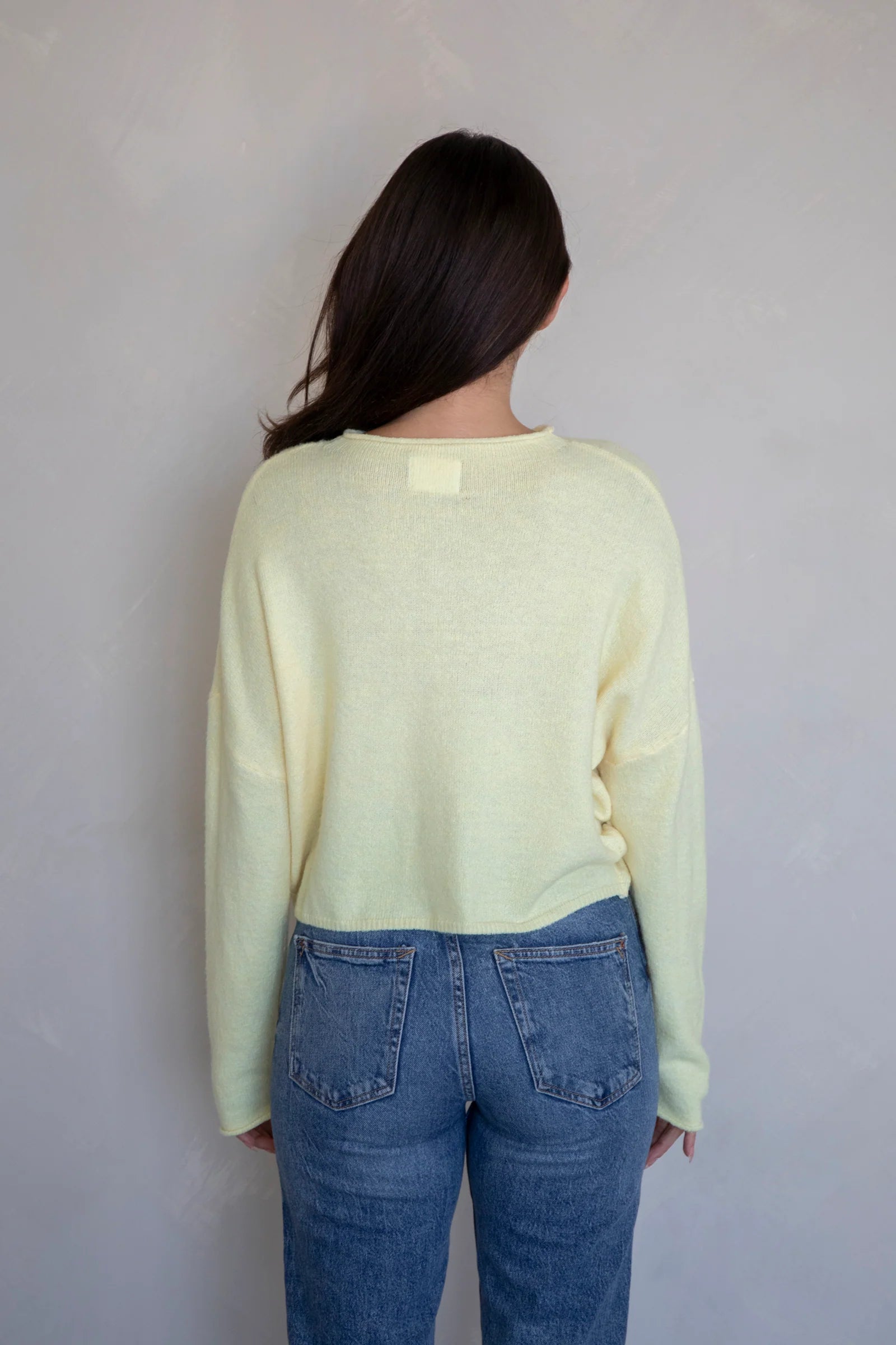 Person wearing a light yellow sweater and blue jeans against a plain background