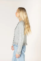 Sterling grey knit cardigan with a crew neckline and button-front closure, featuring delicate ruffle trim along the placket, hem, and cuffs.