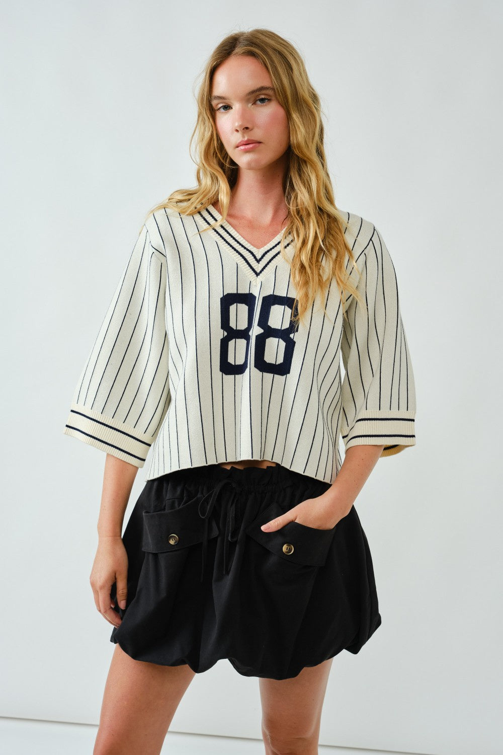Woman wearing a striped baseball jersey with number 88 and black shorts against a white background