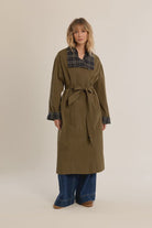 Long belted trench coat featuring a classic plaid lining, wide waist belt, front button closure, and side patch pockets.