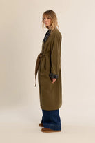Long belted trench coat featuring a classic plaid lining, wide waist belt, front button closure, and side patch pockets.