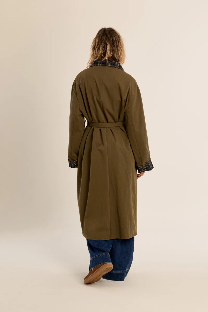 Long belted trench coat featuring a classic plaid lining, wide waist belt, front button closure, and side patch pockets.