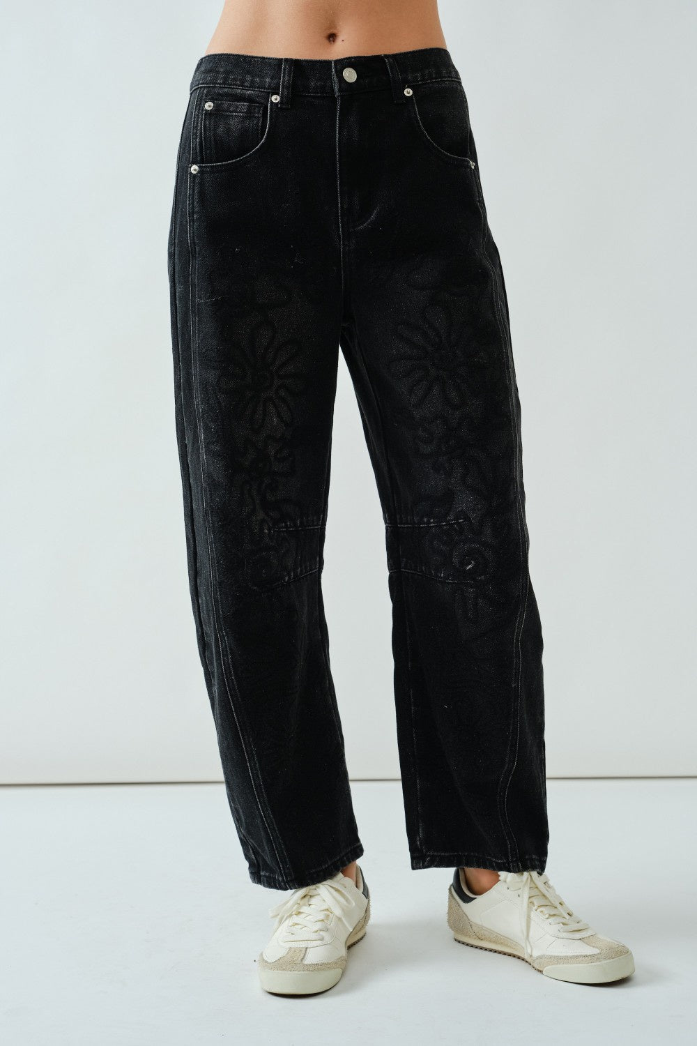 Person wearing black jeans with an embroidered pattern with a plain background