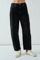 Person wearing black jeans with an embroidered pattern with a plain background