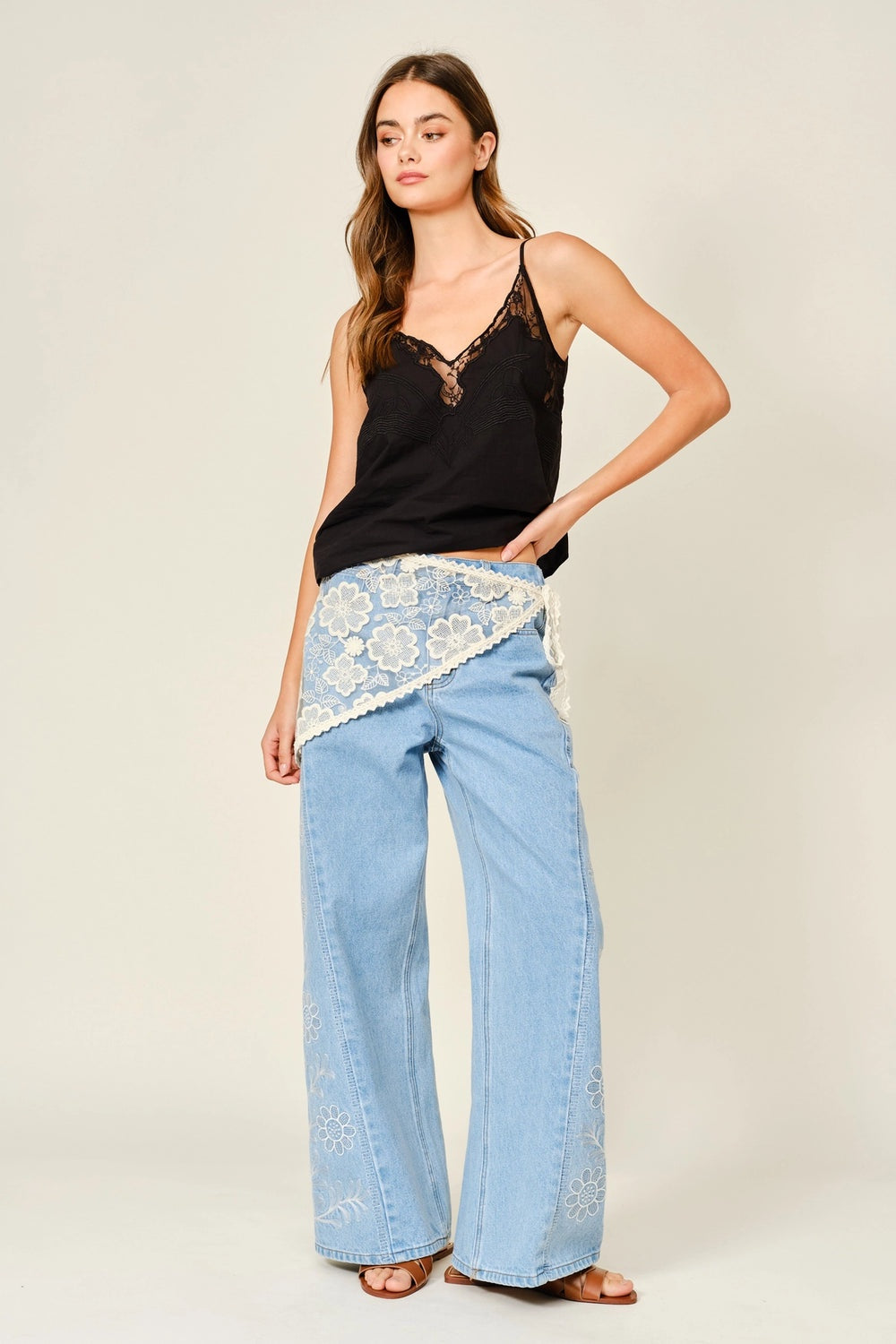 Woman wearing a black top and light blue pants with lace details on a plain background