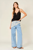 Woman wearing a black top and light blue pants with lace details on a plain background