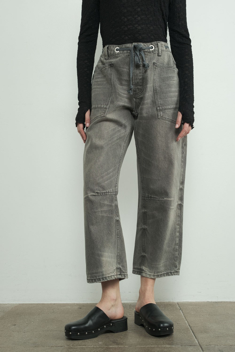 Person wearing dark gray jeans and black clogs on a plain background