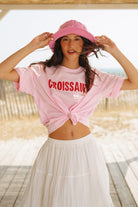 Woman wearing a pink 'Croissant' t-shirt and white skirt outdoors.