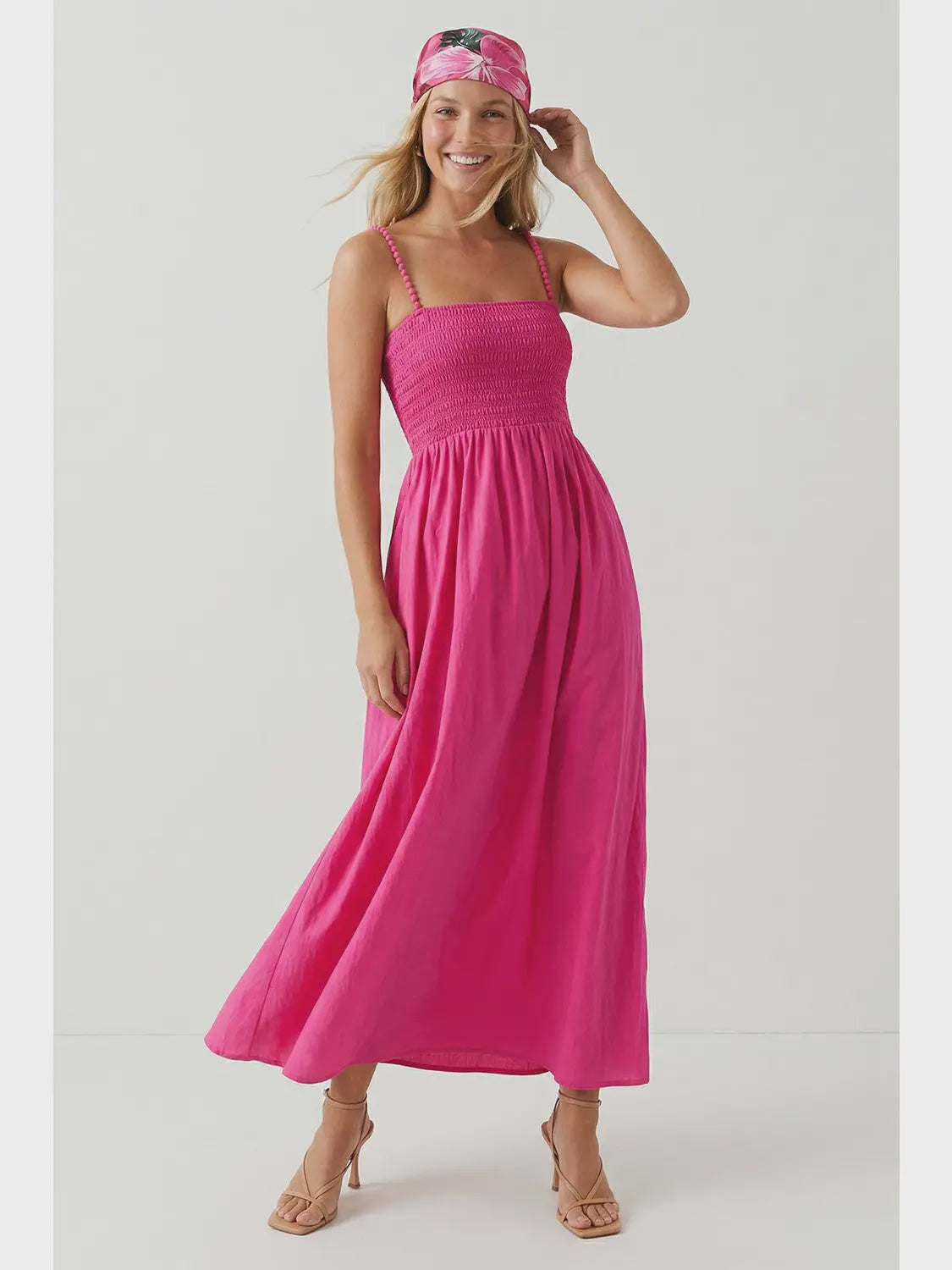 Hot pink maxi dress featuring a fitted smocked bodice, square neckline, adjustable pom pom shoulder straps, a flowing full-length skirt, and side pockets