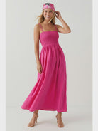 Hot pink maxi dress featuring a fitted smocked bodice, square neckline, adjustable pom pom shoulder straps, a flowing full-length skirt, and side pockets