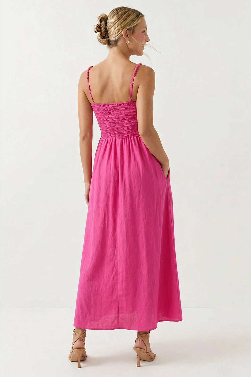 Hot pink maxi dress featuring a fitted smocked bodice, square neckline, adjustable pom pom shoulder straps, a flowing full-length skirt, and side pockets