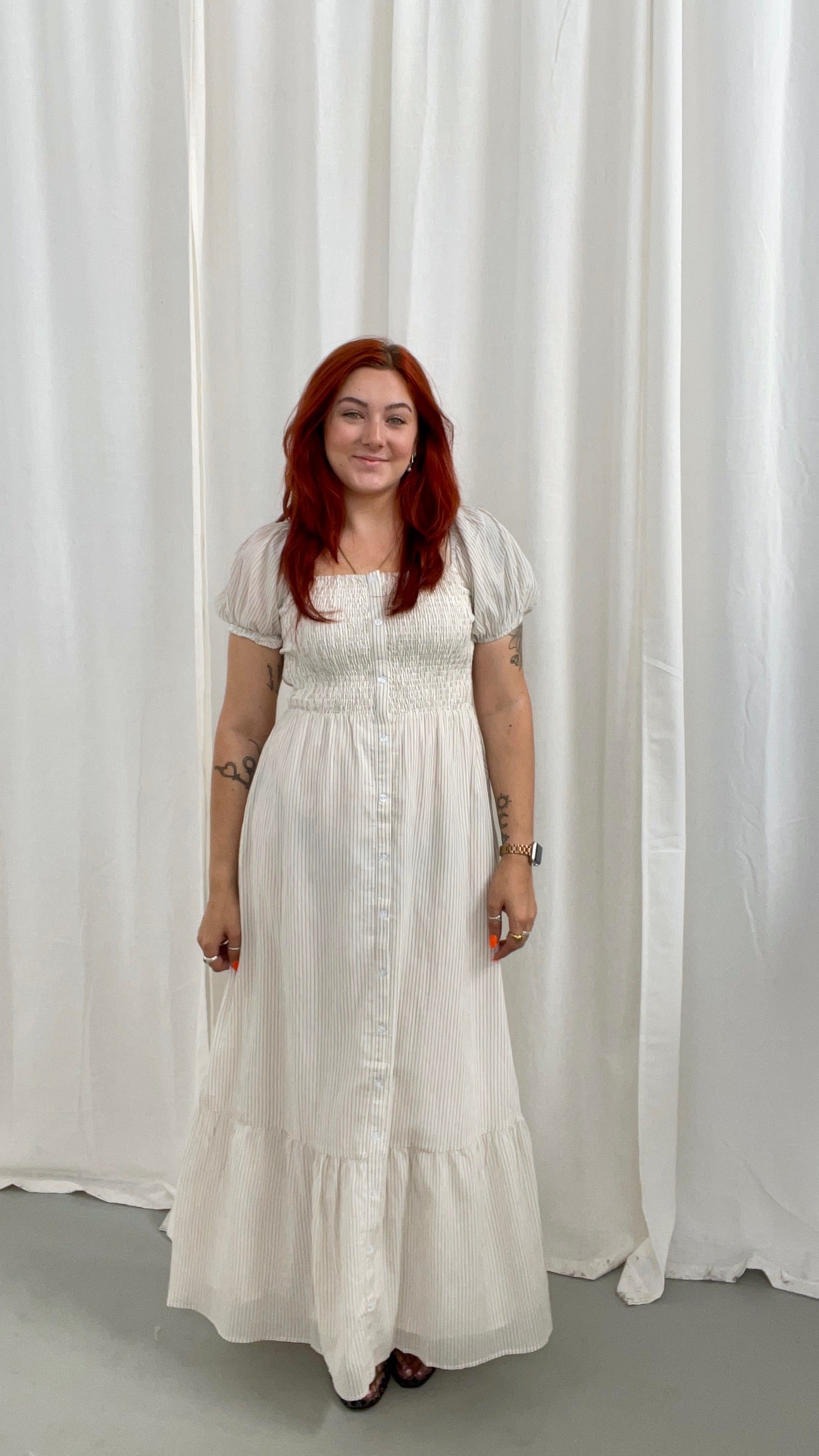 Woman wearing a white dress with light taupe stripes, soft puff sleeves and a button down detail