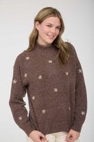 Woman wearing a brown sweater with star flower patterns on a white background