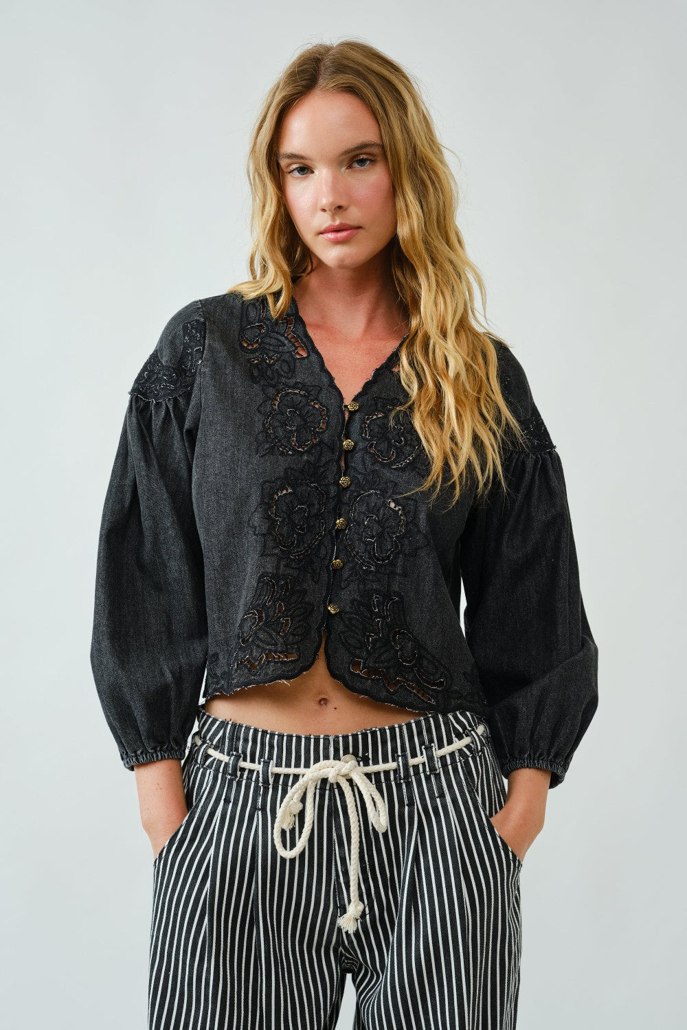 Woman wearing a black embroidered jacket and striped pants against a plain background