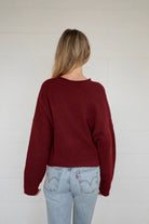 Person wearing a burgundy sweater and light blue jeans against a white wall