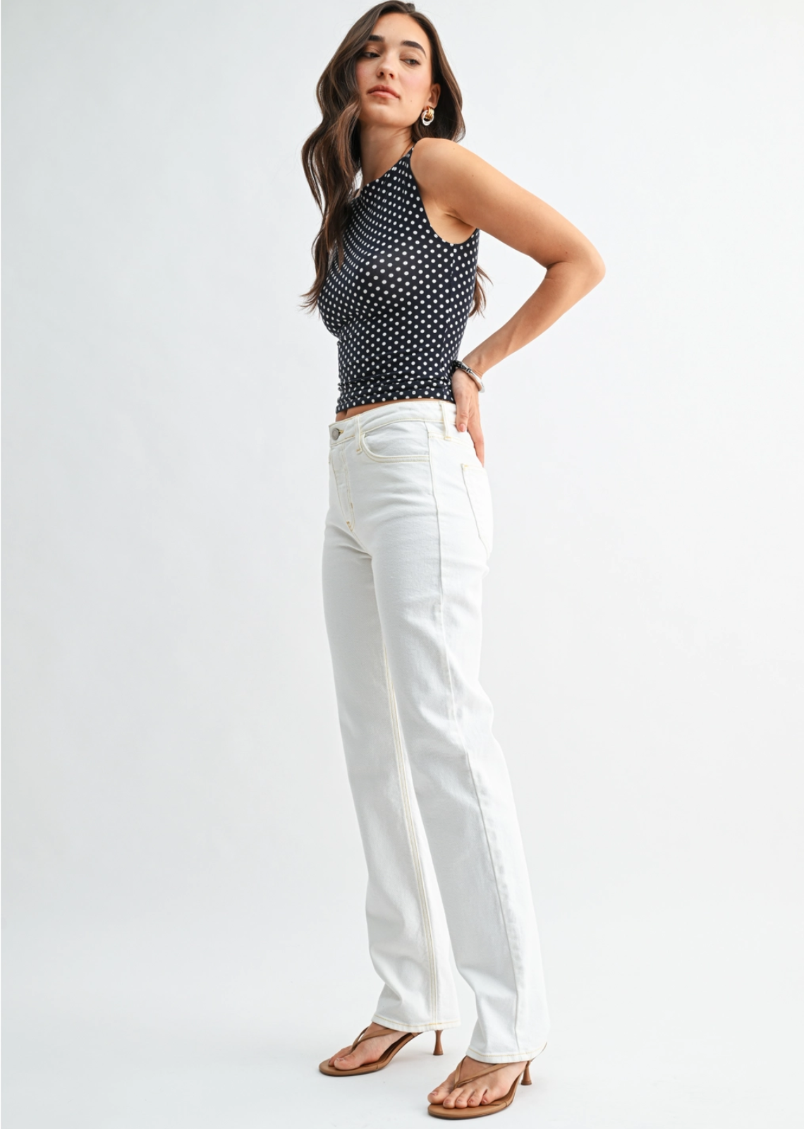 Woman wearing a black polka dot top and white pants on a white background