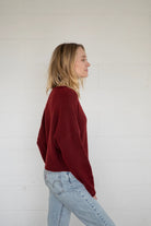 Person wearing a red sweater and light blue jeans against a white wall