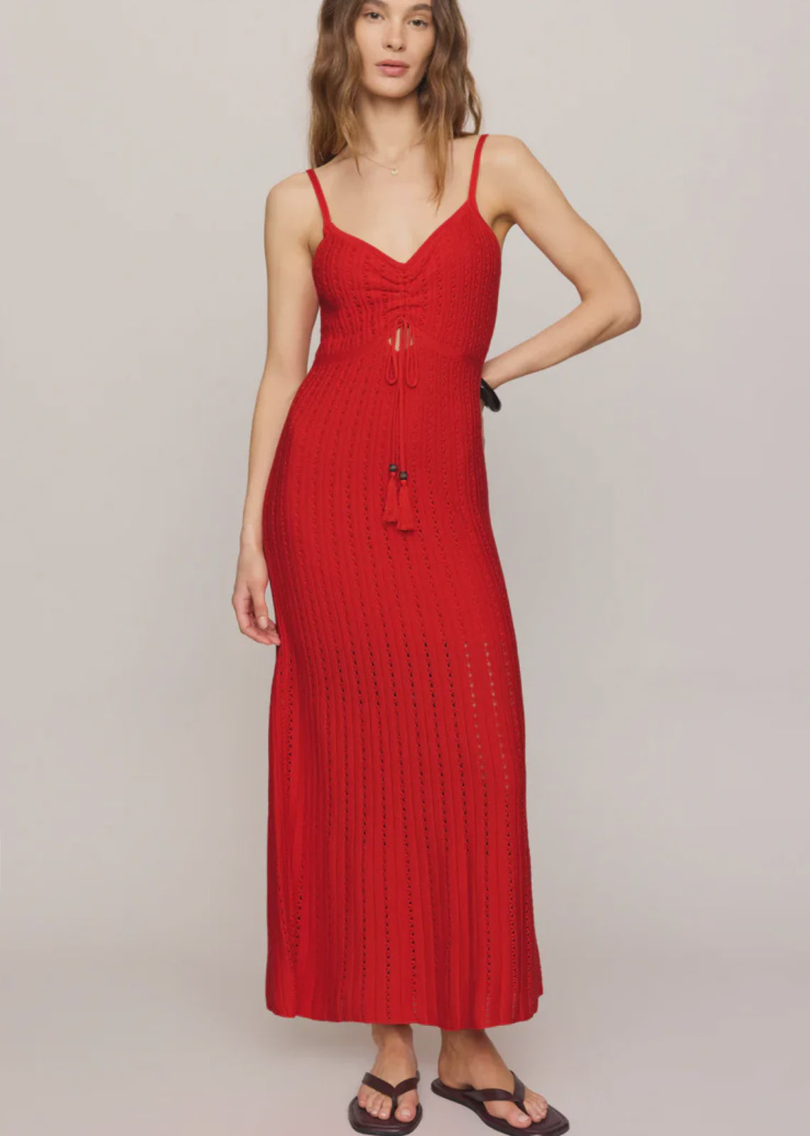 Woman wearing a red crochet dress with tassles against a plain background