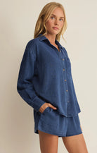 Woman wearing a blue denim shirt and shorts set against a beige background